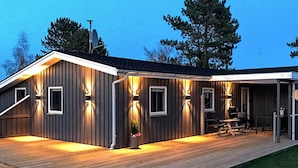 A modern house with a wooden deck, exterior lighting, and a covered patio area. - 4 Star Holiday Home in Haderslev (Haderslev)