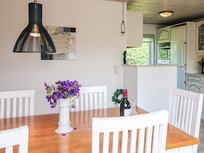 A dining area with a wooden table, white chairs, a vase of purple flowers, a bottle of wine, and a hanging pendant light. - 4 Star Holiday Home in Haderslev (Haderslev)