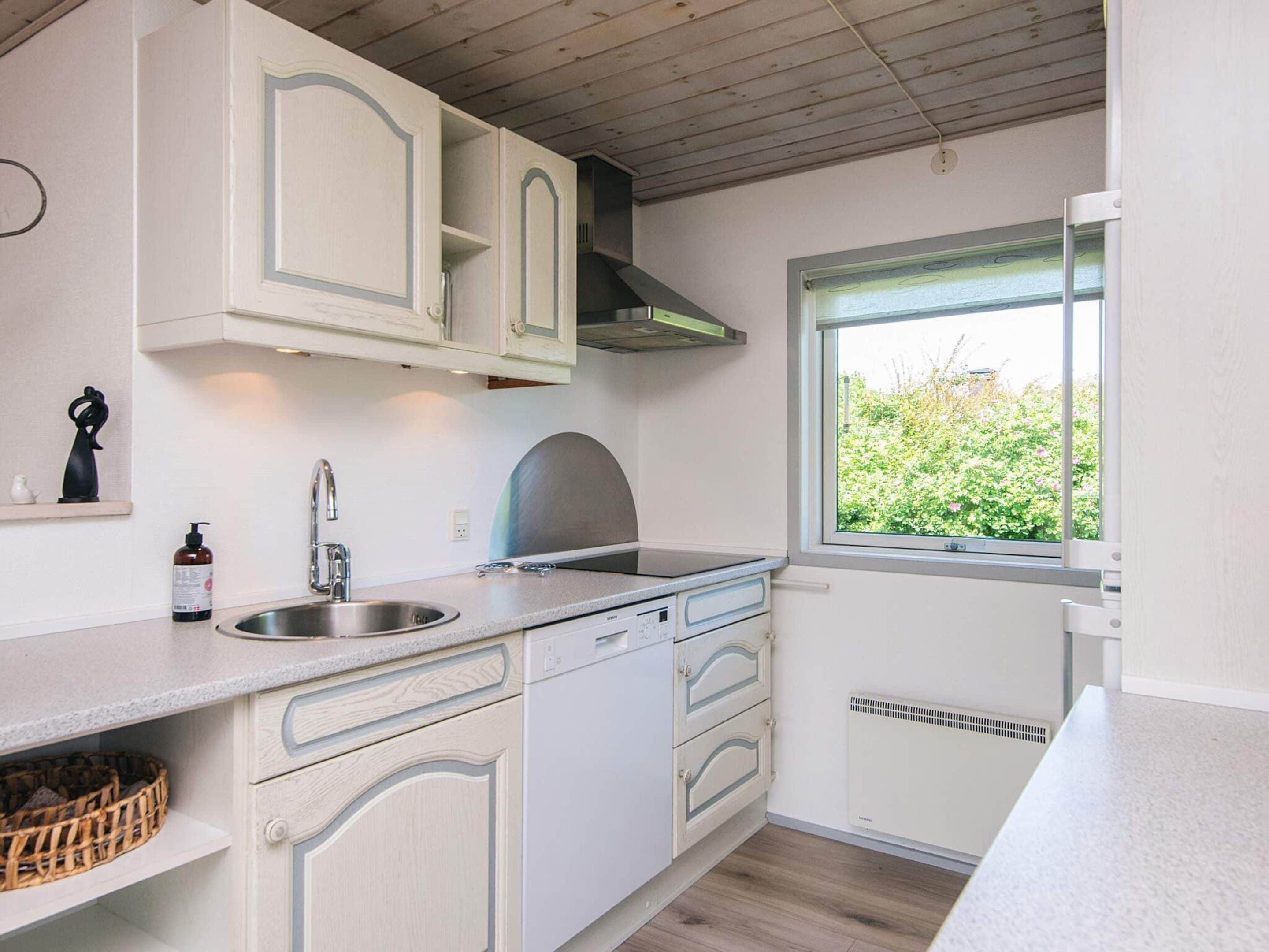 A kitchen with white cabinetry, a stainless steel sink, a window with a view of greenery, and a built-in oven.