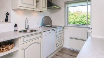 A kitchen with white cabinetry, a stainless steel sink, a window with a view of greenery, and a built-in oven.