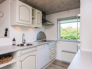 Una cucina con mobili bianchi, lavello in acciaio inossidabile, finestra con vista sul verde e forno integrato.