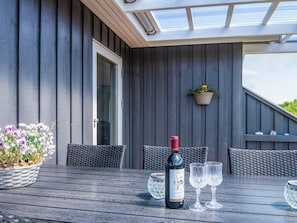 A wooden table with a bottle of wine and two glasses, a wicker chair, and a hanging plant. - 4 Star Holiday Home in Haderslev (Haderslev)