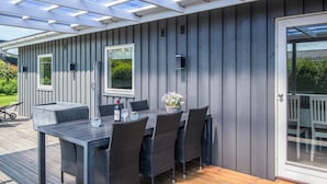 A covered patio with a table and chairs, a glass door, and a view of greenery. - 4 Star Holiday Home in Haderslev (Haderslev)