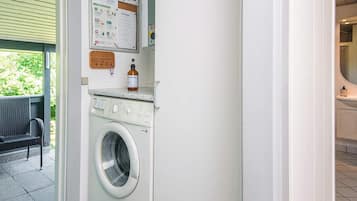Een wasserette met een wasmachine, een prikbord met mededelingen en een fles wasmiddel.