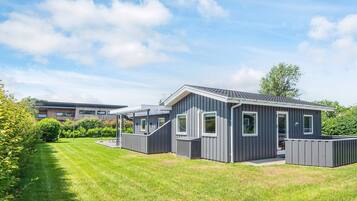 A modern mobile home with a covered patio, a well-maintained lawn, and a clear sky.