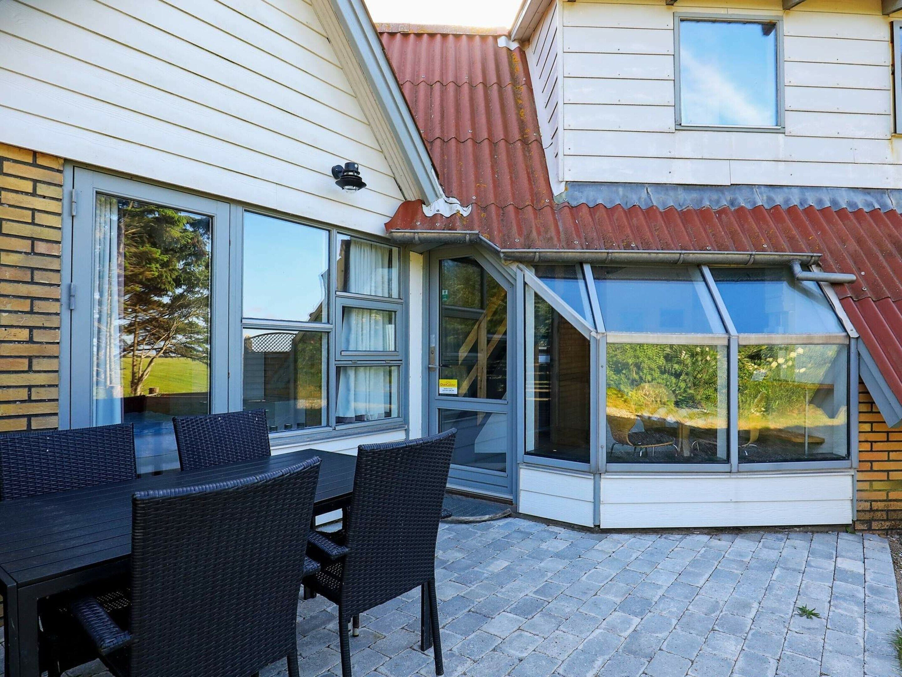 A corner patio with a glass enclosure, wicker furniture, and a brick wall.