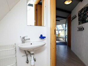 A modern bathroom with a white sink, a mirror, and a wooden door leading to a hallway.