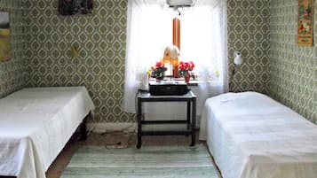 A room with two single beds, a small table with a lamp, and a window with a view of the outside.