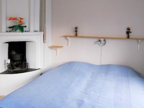 A bedroom with a bed, a fireplace, and two wall-mounted shelves with flowers. - 6 Person Holiday Home in Ryssby (Ryssby)