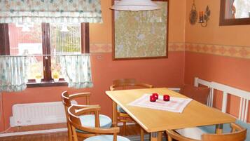 A dining area with a wooden table and chairs, a radiator, a window with curtains, and a wall-mounted lamp.