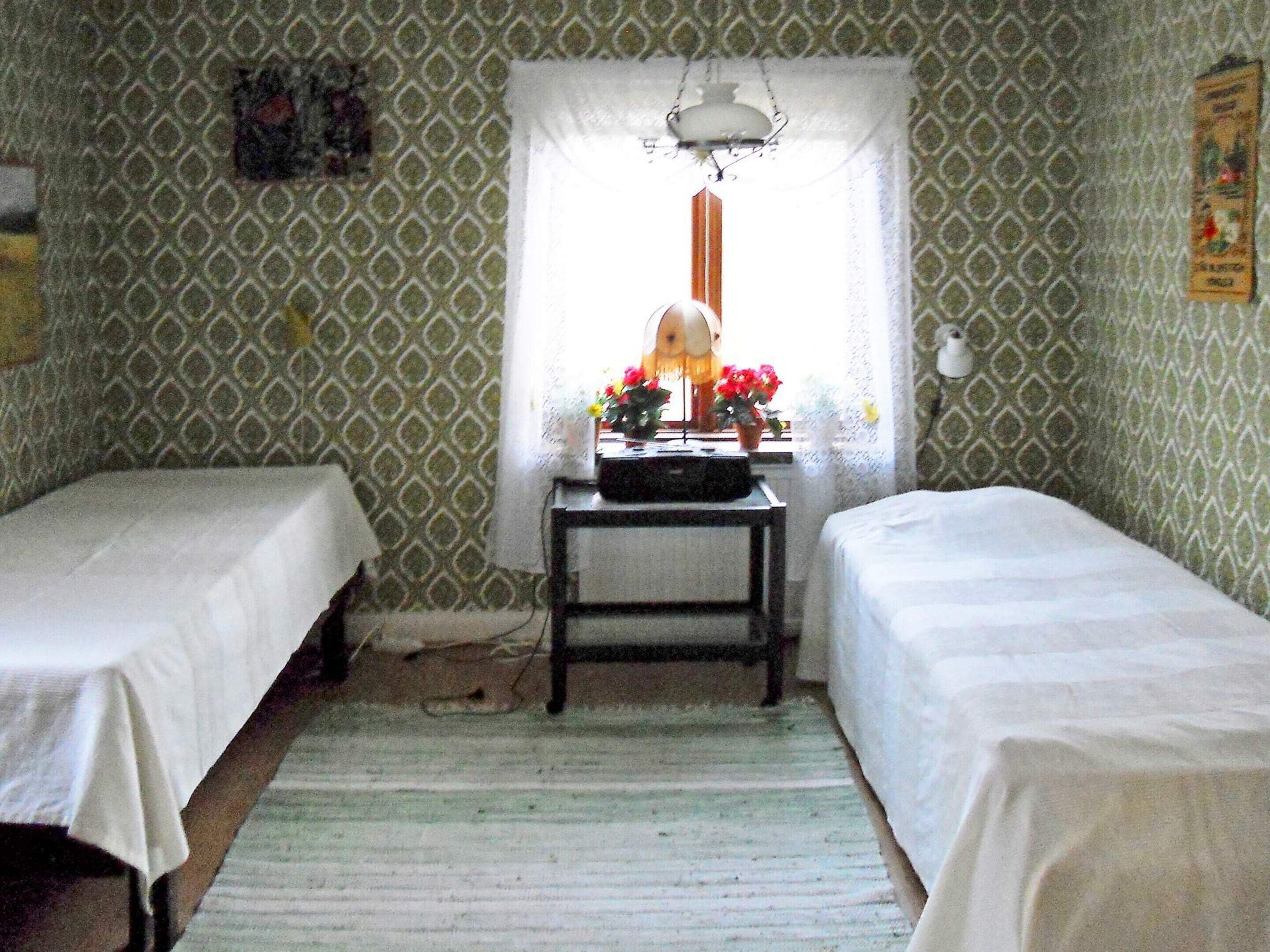 A room with two single beds, a small table with a lamp, and a window with a view of the outside.