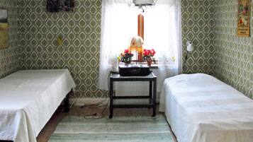 A room with two single beds, a small table with a lamp, and a window with a view of the outside.
