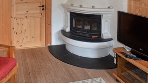 Ein gemütliches Wohnzimmer mit Kamin, Holzboden, Fernseher und einem roten Sessel.