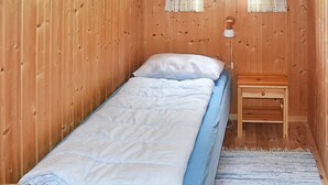 Ein kleines Zimmer mit einem Einzelbett, einer Holzwand, einem kleinen Nachttisch und einer Lampe.