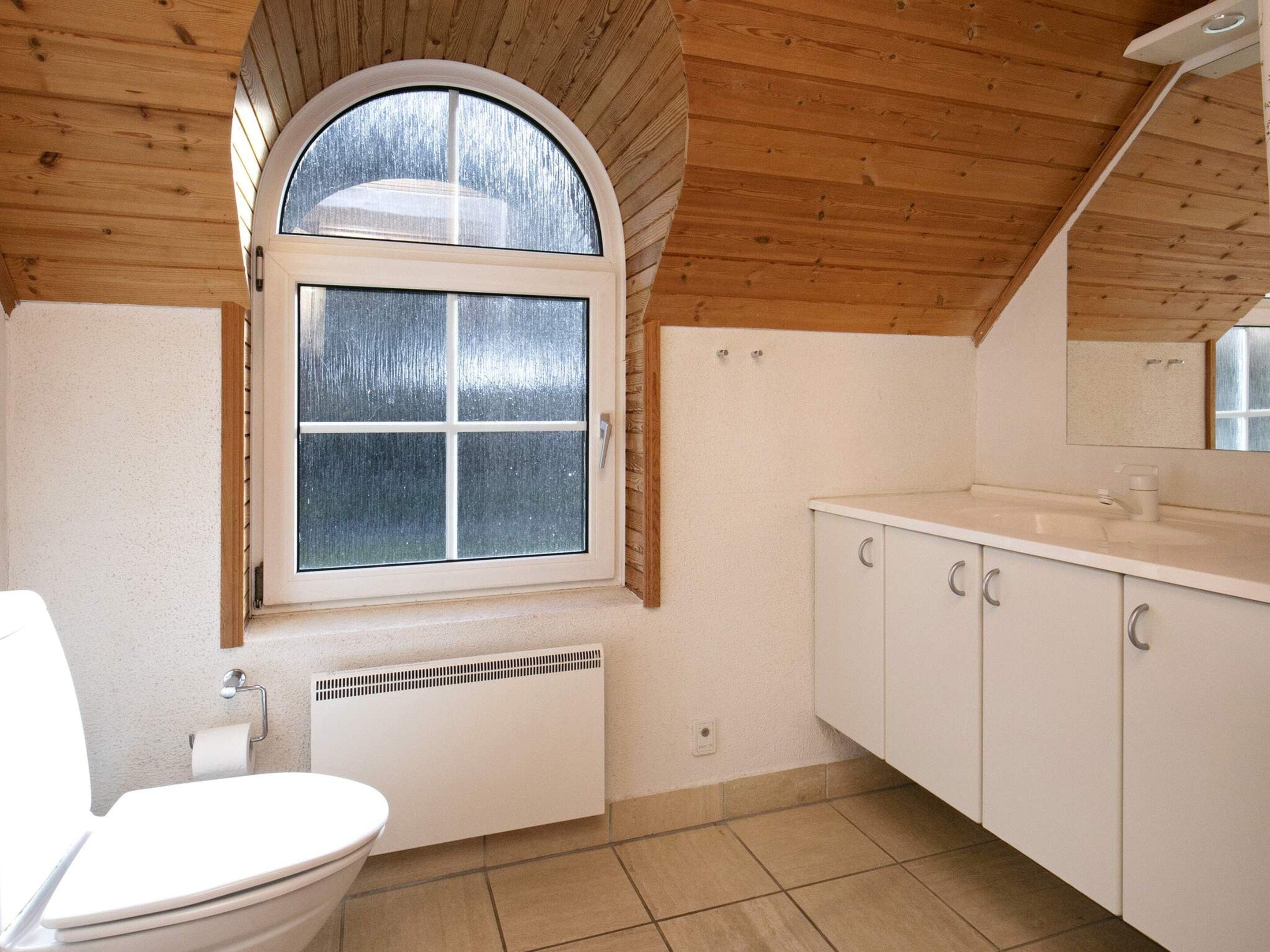 Ein Badezimmer mit einer weißen Toilette, einem Fenster mit Aussicht und einem weißen Waschbecken mit Schränken.