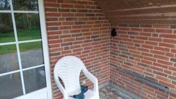A room with a brick wall, a white plastic chair, and a window.