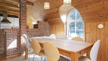 A wooden interior with a brick fireplace, a dining table with chairs, and a large window.