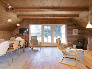 Un intérieur chaleureux en bois, comprenant un coin repas, des sièges, une cheminée et un téléviseur.