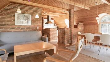 A rustic interior with a brick fireplace, wooden ceiling beams, and a seating area with a table and chairs.