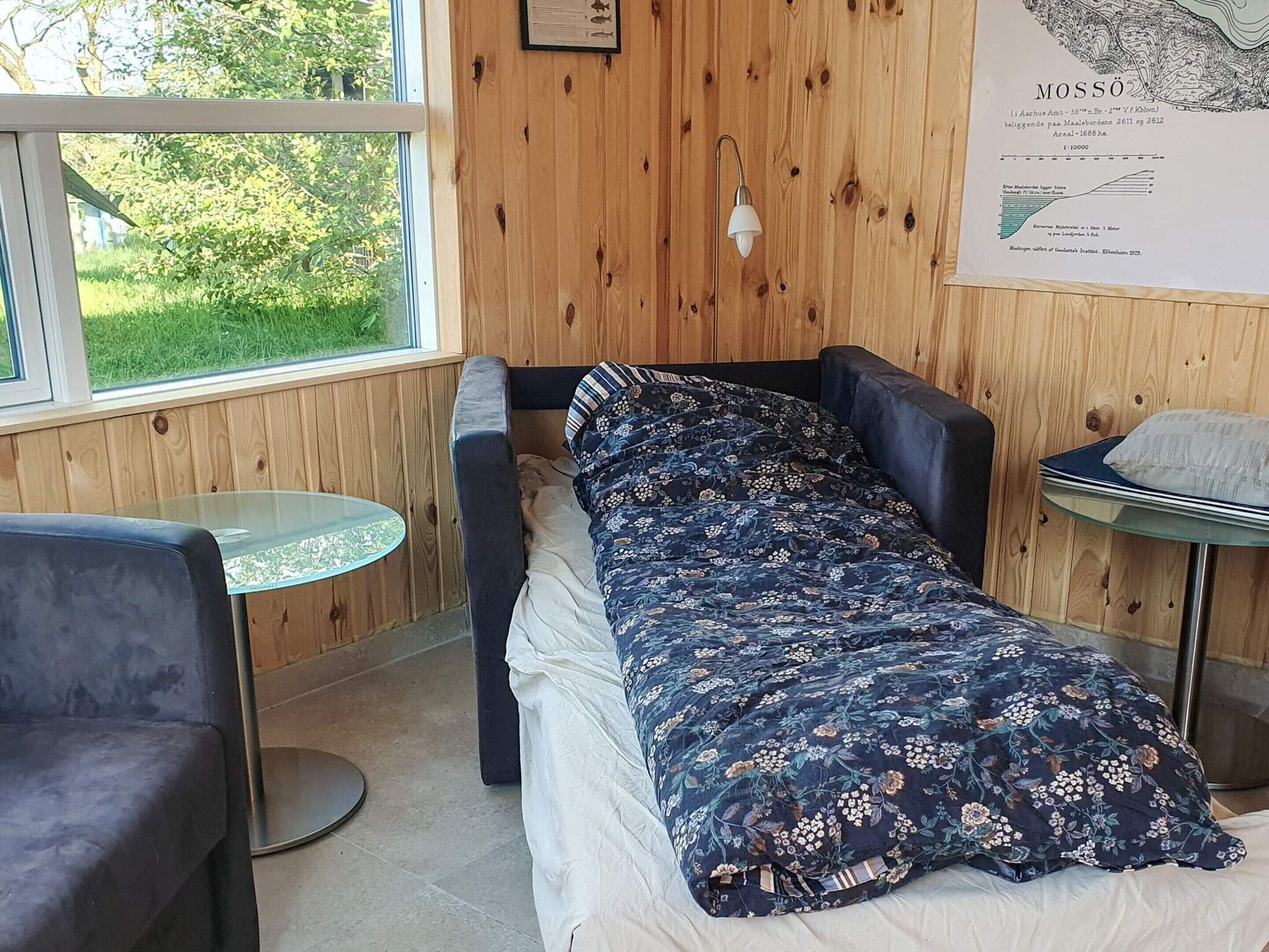A room with a bed, a small round table, a chair, and a window with a view of greenery.