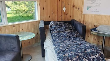 A room with a bed, a small round table, a chair, and a window with a view of greenery.