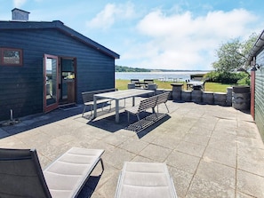 A patio with a table and benches, a small building with a door, and a view of a body of water. - Spacious Holiday Home in Storvorde With Sea Nearby (Skanderborg)