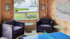 Una habitació amb dues butaques de pell, una taula de ping-pong i una finestra gran amb vista a un llac.