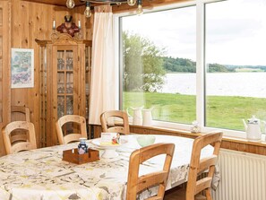 A dining area with a table set for four, wooden chairs, a cabinet with glass doors, and a view of a lake through large windows. - Spacious Holiday Home in Storvorde With Sea Nearby (Skanderborg)