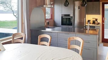 Una cocina moderna con gabinetes grises, electrodomésticos de acero inoxidable y una zona de comedor con una mesa redonda y sillas de madera.