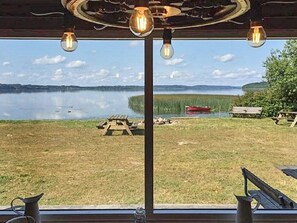 A lakeside view from a cabin with a wooden deck, picnic table, and a boat in the distance.