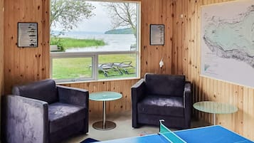 Una stanza con due poltrone in pelle, un tavolo da ping pong e un'ampia finestra con vista su un lago.