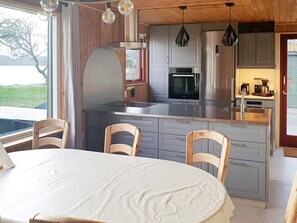 A modern kitchen with grey cabinets, stainless steel appliances, and a dining area with a round table and wooden chairs. - Spacious Holiday Home in Storvorde With Sea Nearby (Skanderborg)