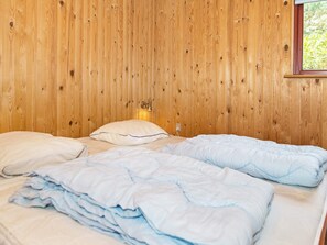 A room with wooden panel walls, two beds with white and light blue bedding, and a wall-mounted light fixture.