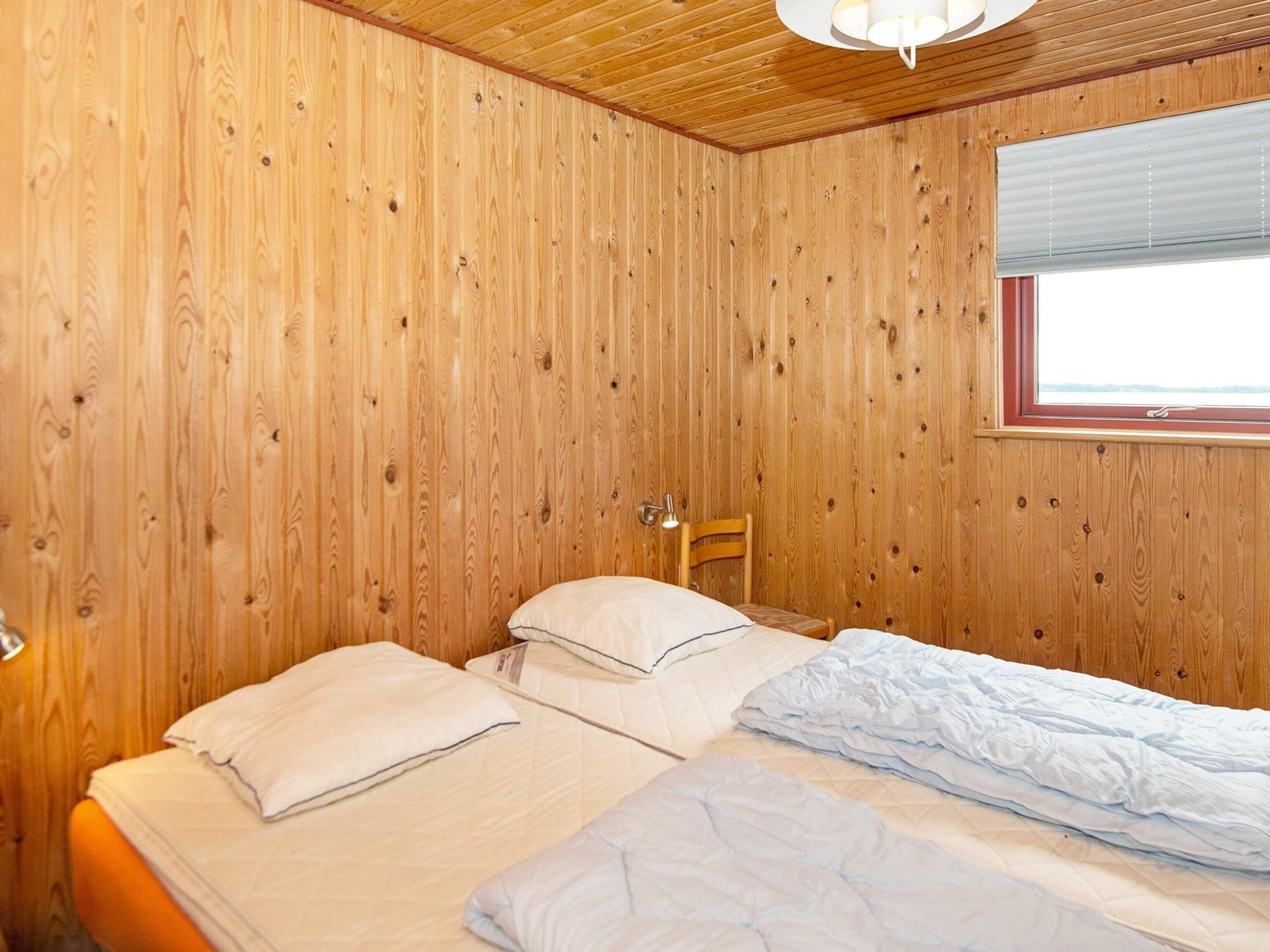 Een kamer met houten lambrisering, een bed, een stoel en een raam met zonwering.