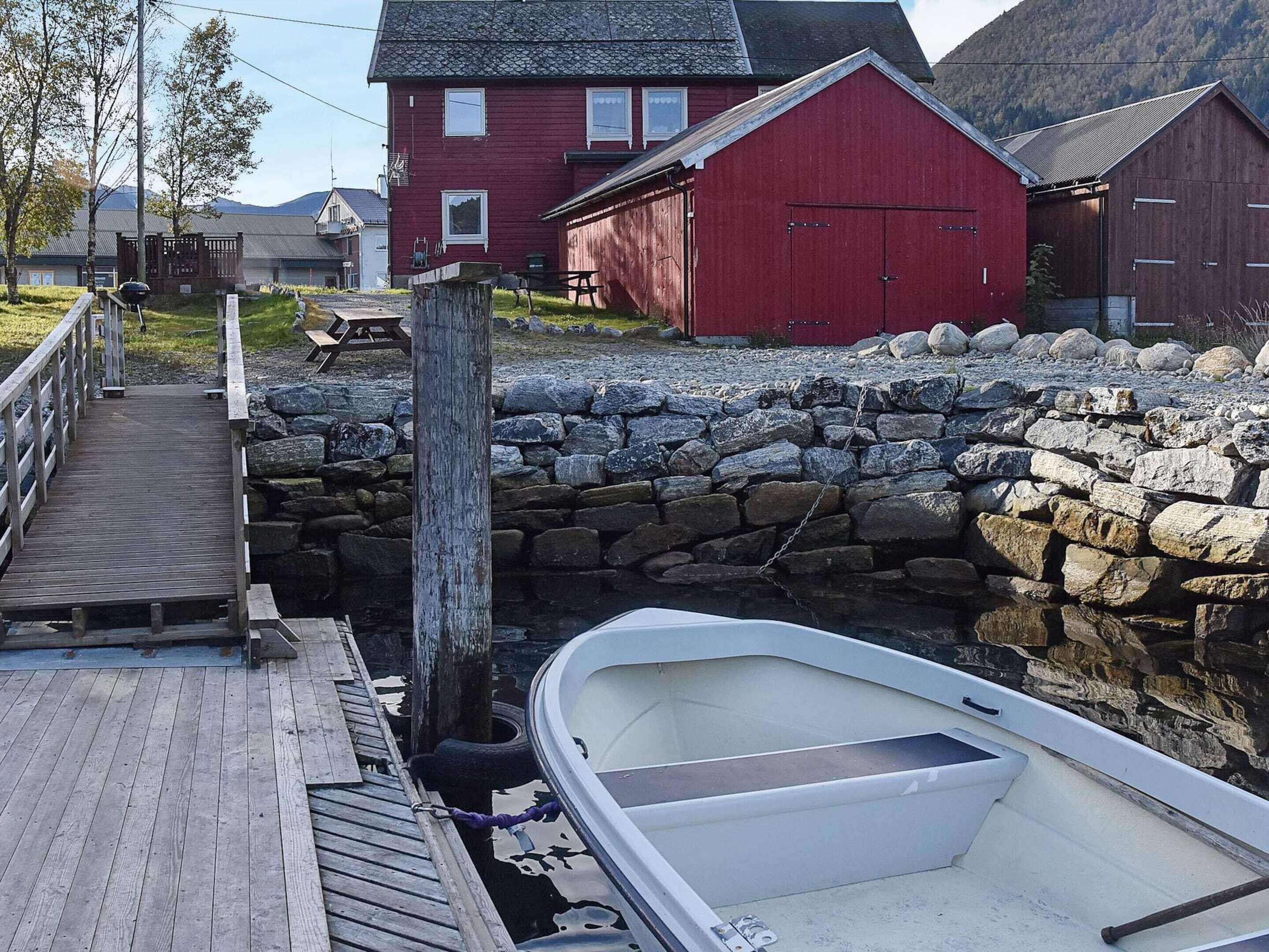 A wooden dock leading to a stone wall, a red building, and a white boat.