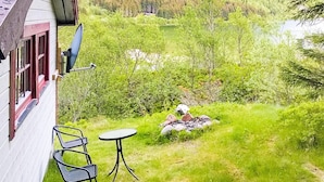 A patio with two metal chairs and a small round table, surrounded by lush green grass and a small rock formation. - 5 Person Holiday Home in Engavagen (Meloy)