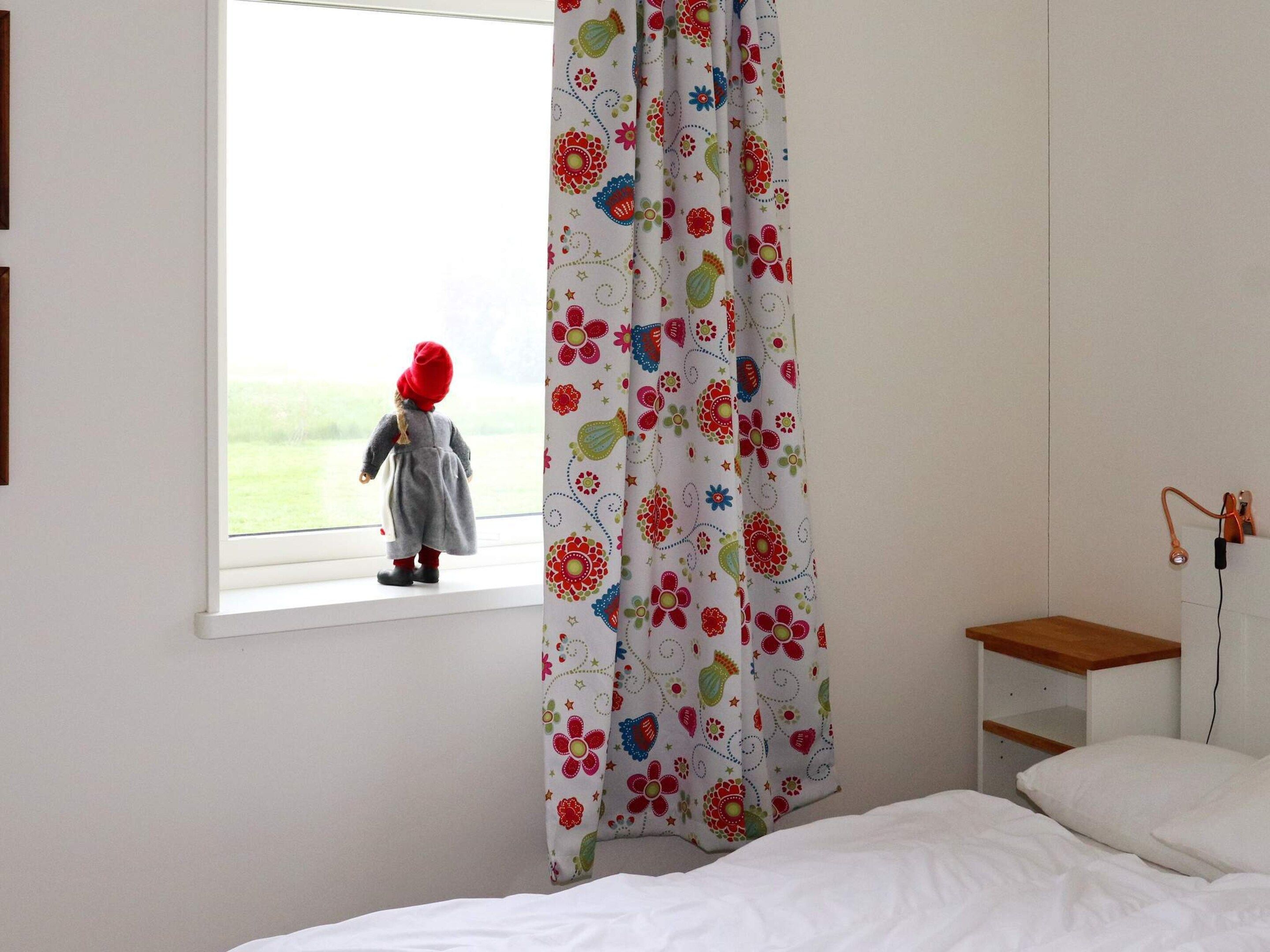 Ein Zimmer mit Fenster, einem Bett, einem Nachttisch und einem Vorhang mit Blumenmuster.