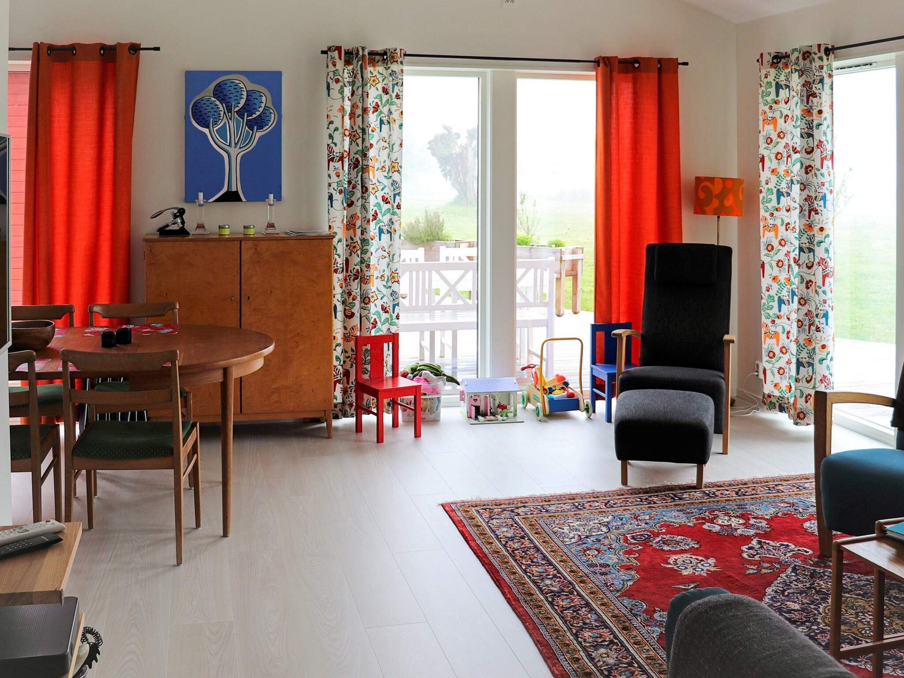 Una sala de estar con comedor, un sofá, un tapete rojo y vistas al exterior.