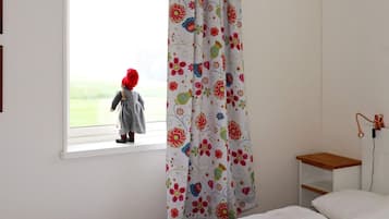 Una habitación infantil con ventana, cama, mesita de noche y cortina estampada con motivos florales.