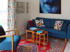 Ein Wohnzimmer mit einem blauen Sofa, gemusterten Kissen, einem Holztisch und einem farbenfrohen Teppich.