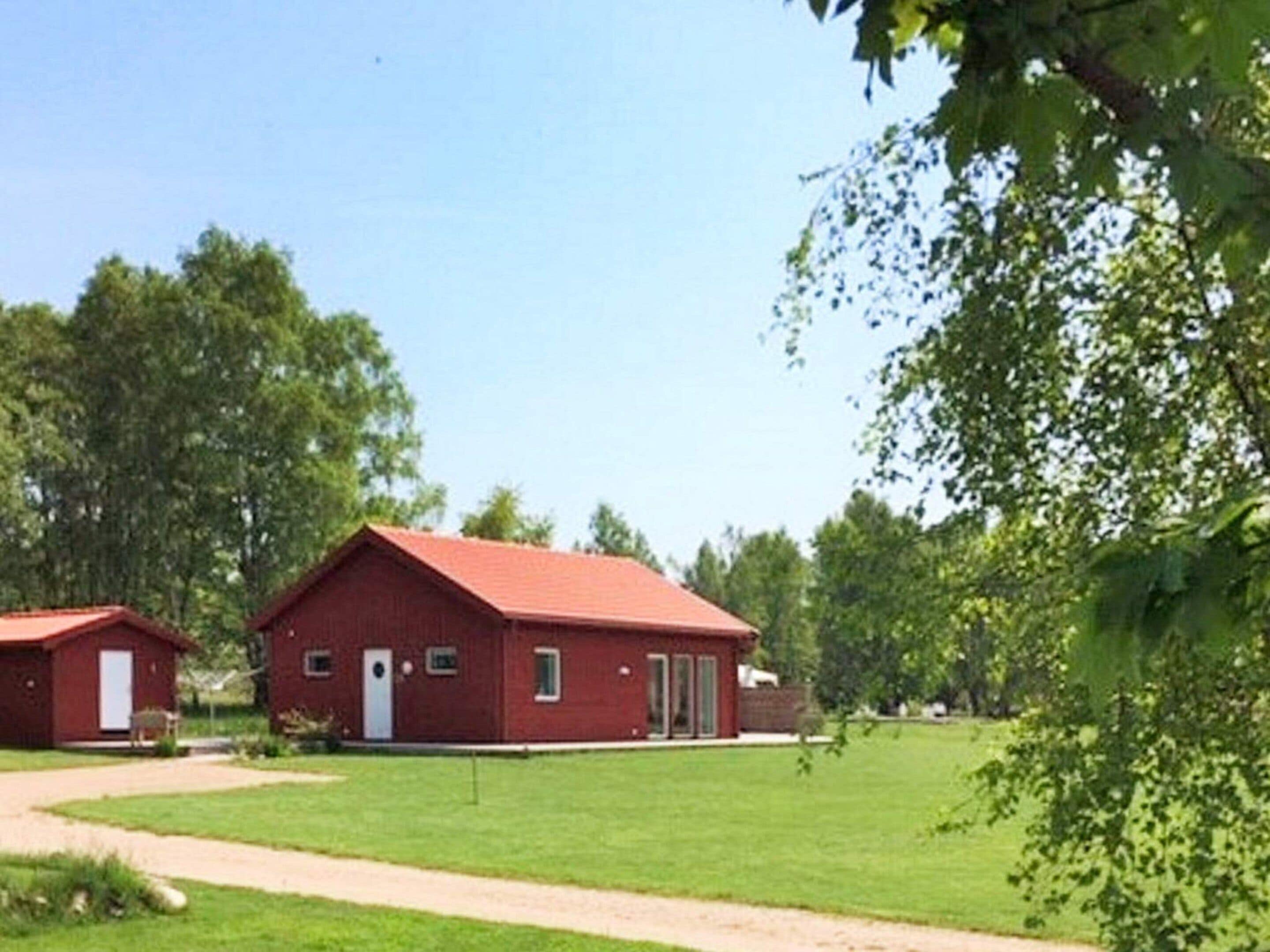 A red building with a door and windows, surrounded by green grass and trees.