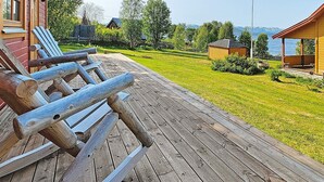 Eine Holzterrasse mit Adirondack-Stühlen, ein Rasen und der Blick auf einen See und Berge.