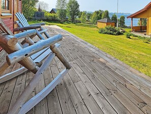 Eine Holzterrasse mit Adirondack-Stühlen, ein Rasen und der Blick auf einen See und Berge.