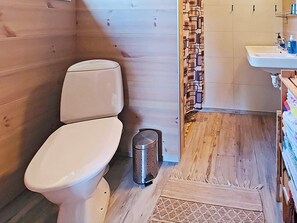 Une salle de bain aux murs lambrissés, équipée de toilettes, d’un lavabo et d’une poubelle.