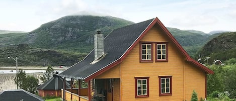 A wooden house with a gabled roof, a chimney, and a porch with chairs.