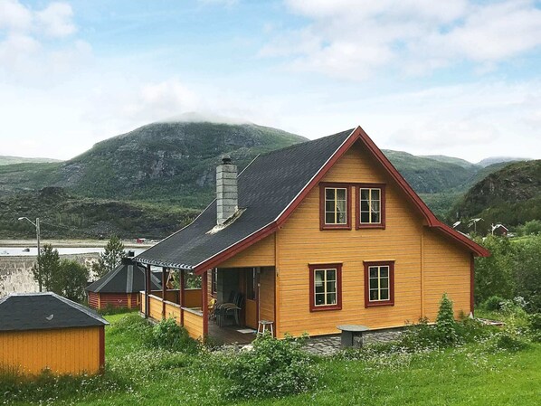 Une maison en bois avec un toit à pignon, une cheminée et une véranda avec des chaises.