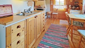 L’intérieur d’un chalet en bois comprend un coin cuisine avec des meubles de rangement en bois, un évier et une table à manger avec des chaises.