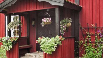 A red wooden house with a porch, stone steps, and hanging flower baskets.