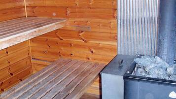 A sauna room with wooden walls, a bench, and a metal heater.