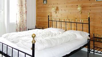 A bed with a metal frame and gold accents, a wooden headboard, and a window with floral curtains.